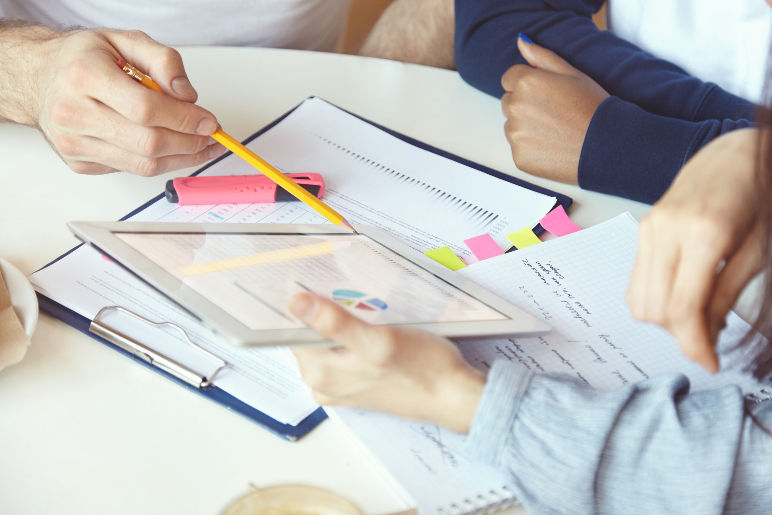 Working in team: young businesspeople discussing business plans and ideas, analyzing graphics and diagrams on paper. Man holding pen, pointing at tablet pc screen, explaining project strategy